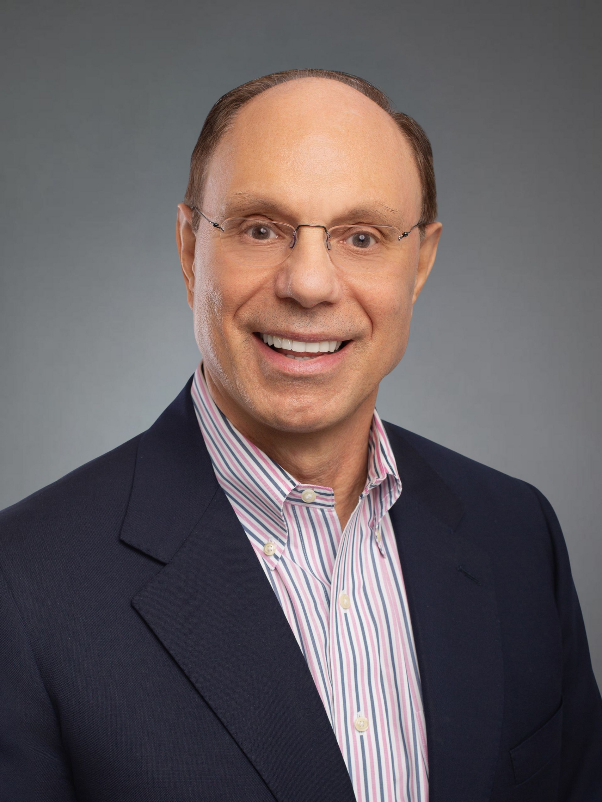 Man in blue blazer and glasses smiles, indoors.