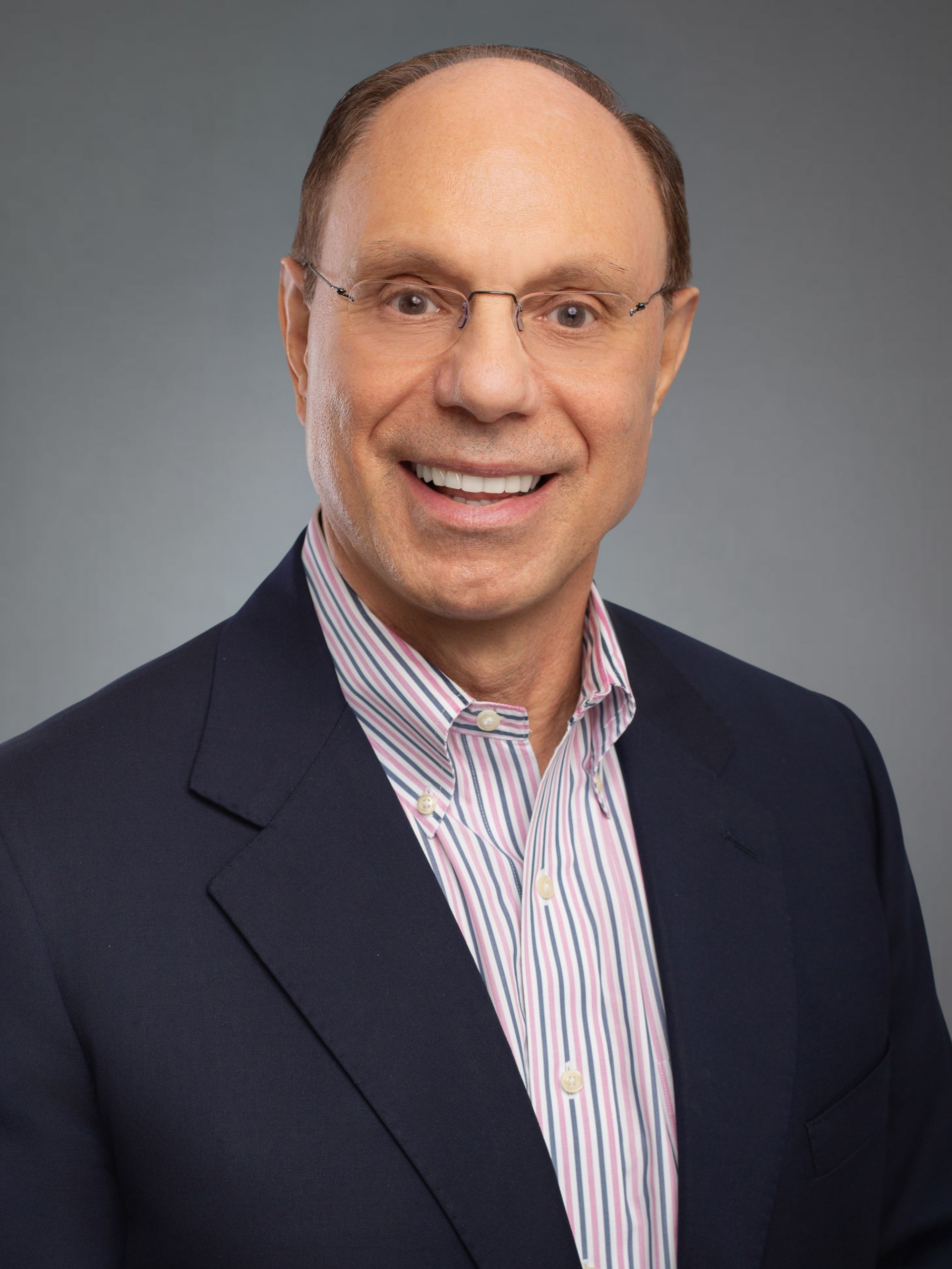 Man wearing glasses, blue blazer over a light pinstriped shirt, smiling, neutral background.