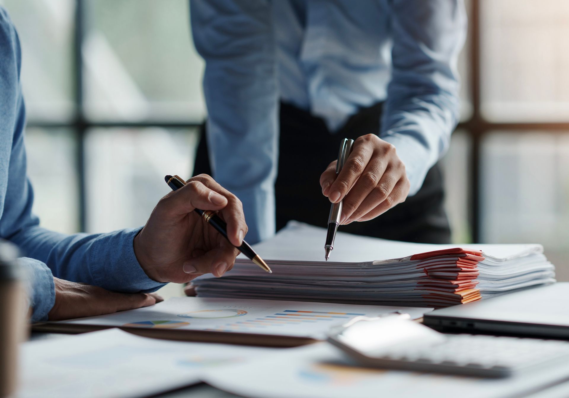Two people review documents at a desk, one pointing with a pen.