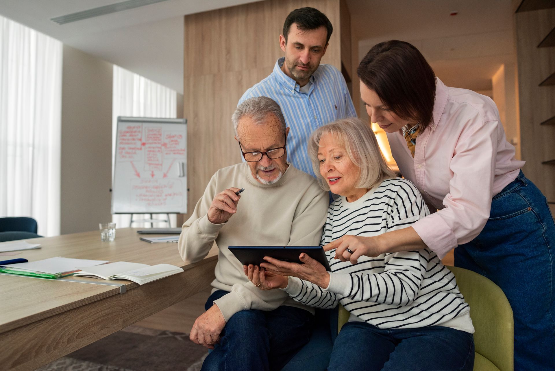Four people reviewing tablet in a bright office. Woman points, man gestures, others look on.