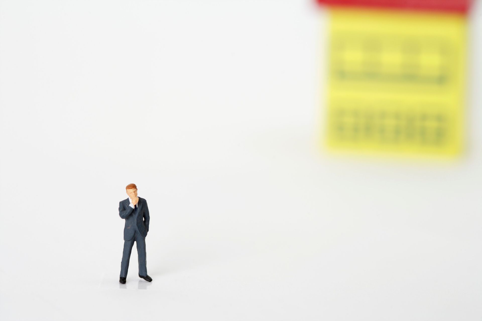 A small figurine of a businessman in a dark suit standing on a white surface.