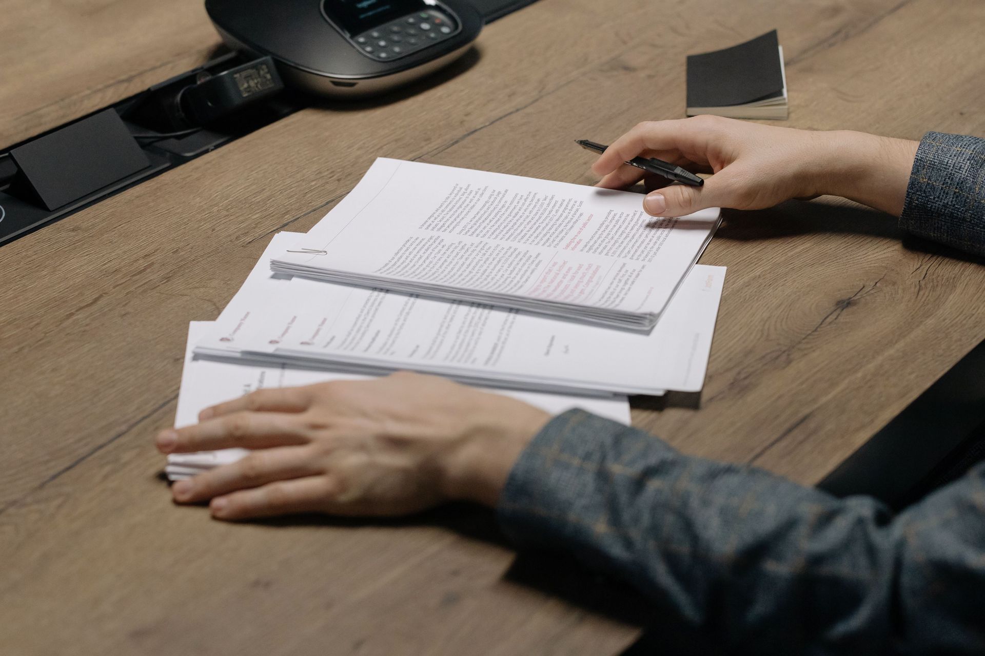 A person reviewing paperwork and holding a pen at a wooden conference table in a professional office