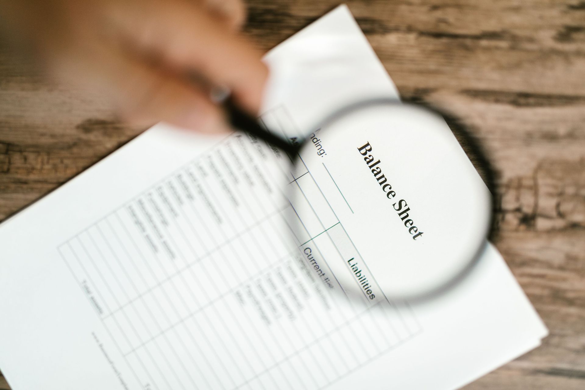 A person using a magnifying glass to examine a printed financial document labeled 