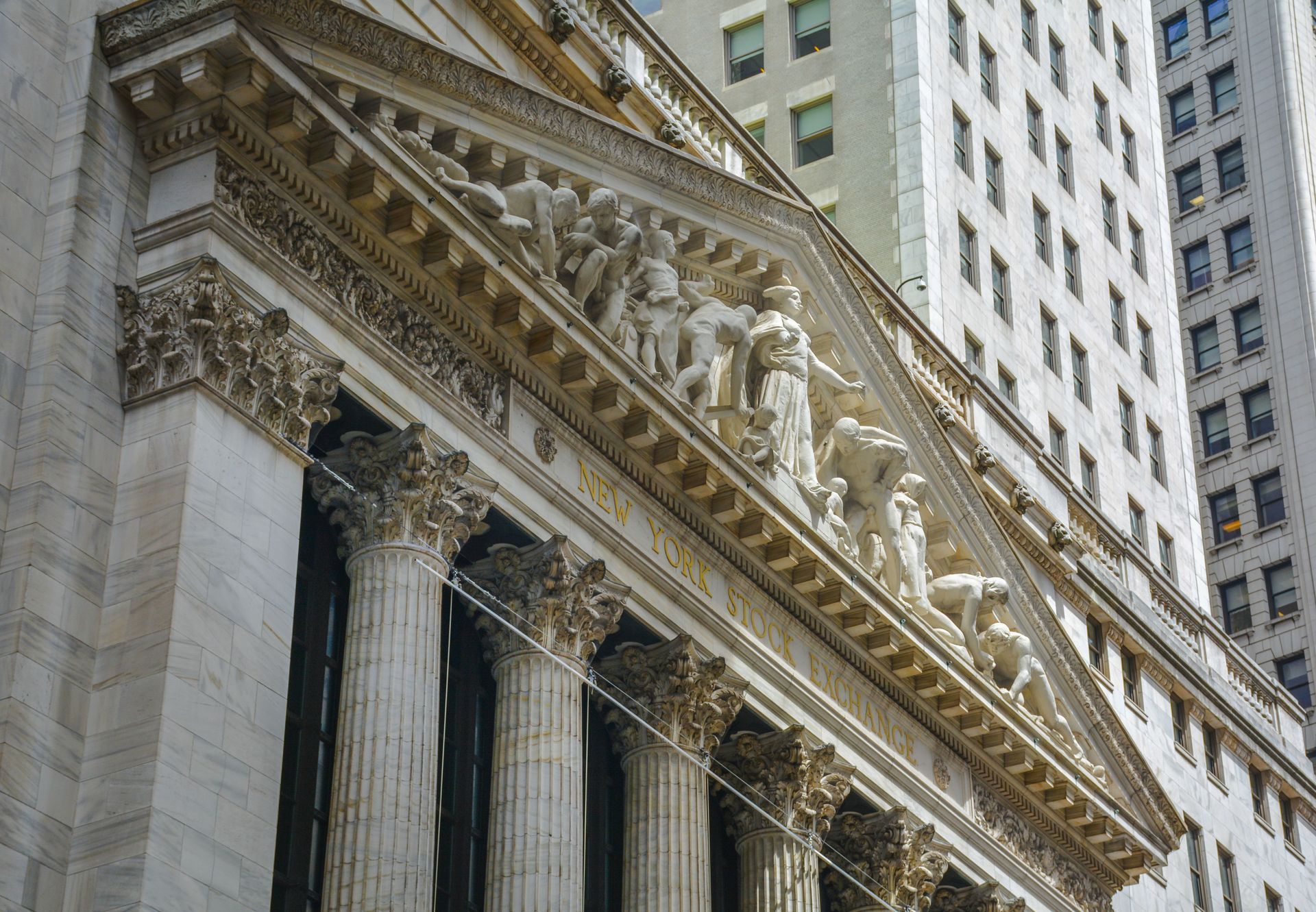 The image shows the historic facade and pediment sculpture of the New York Stock Exchange building.