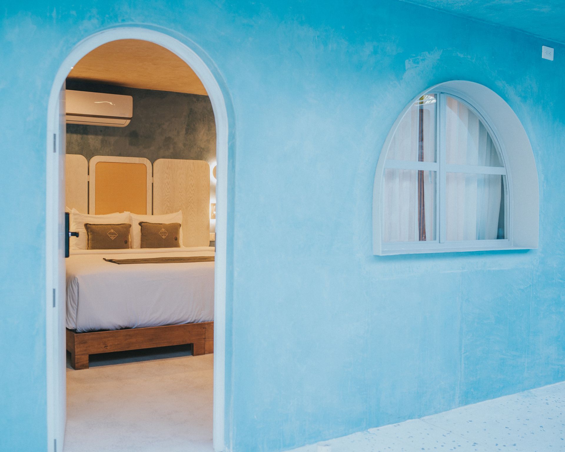Pasillo de estuco azul con puerta arqueada que da a un dormitorio, ventana arqueada con marco blanco.