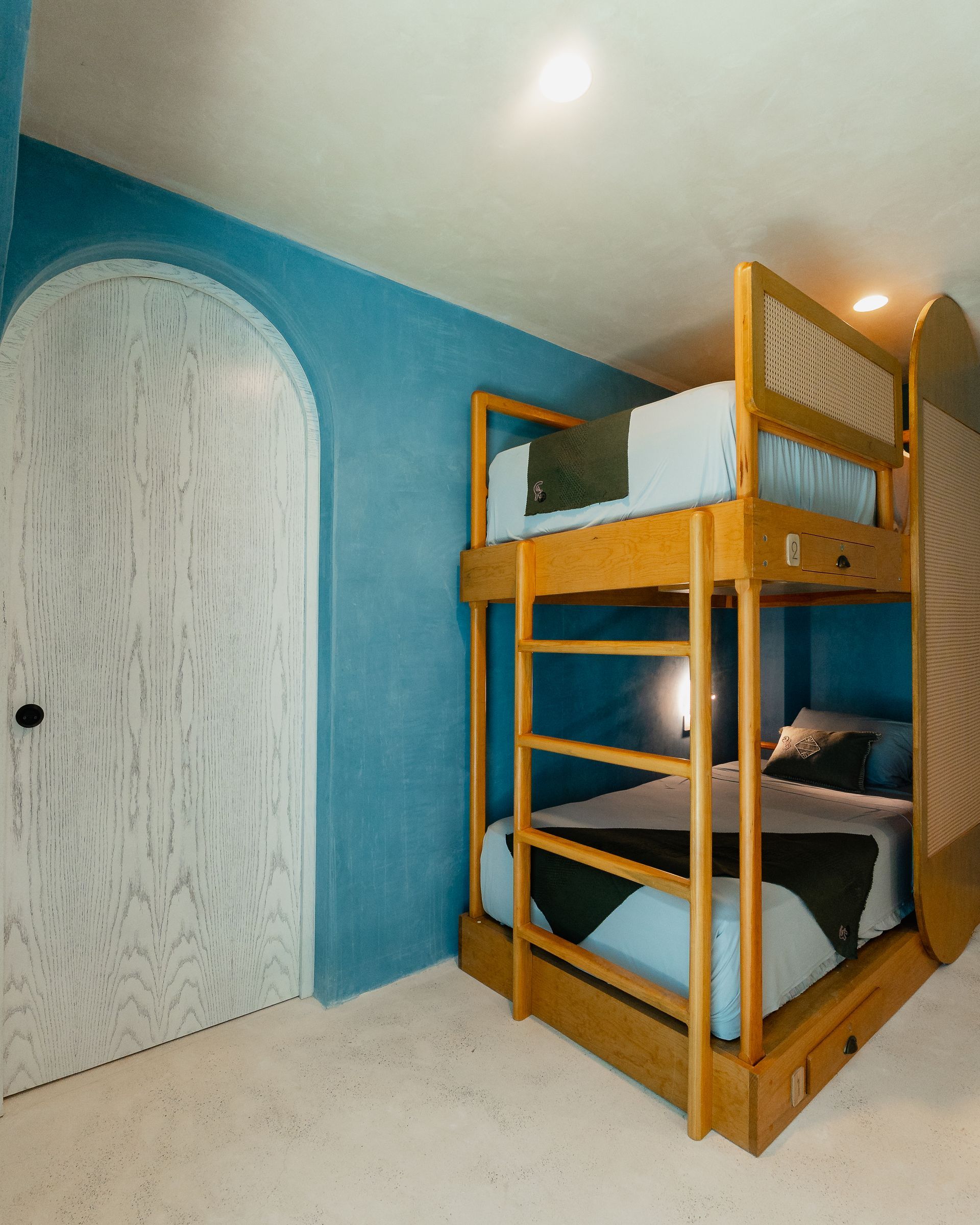 Literas de madera en una habitación azul con puerta arqueada y suelo blanco.
