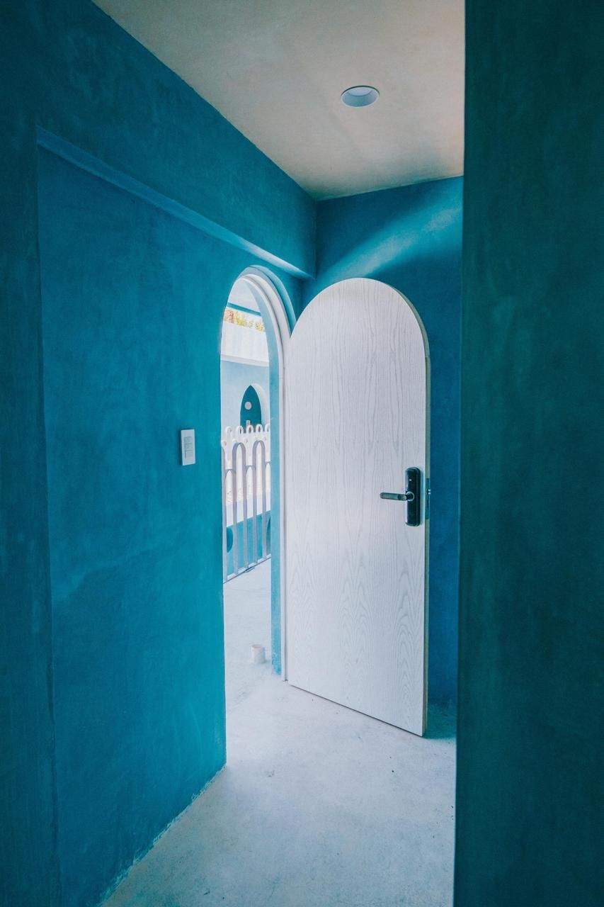 Pasillo azul con puertas arqueadas y una puerta blanca.
