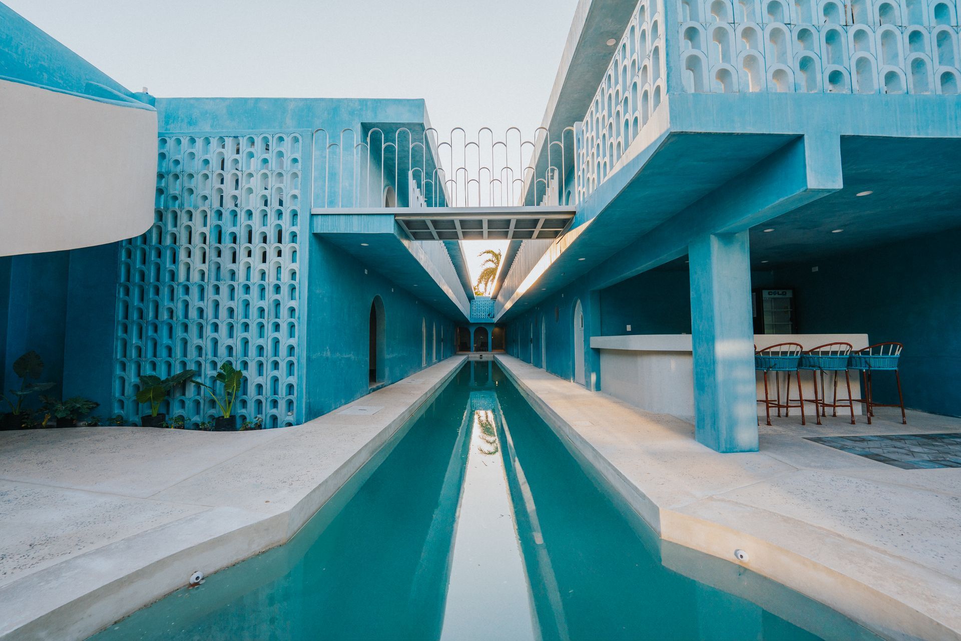 Complejo arquitectónico de color turquesa con un largo estanque reflectante, bar al aire libre y una pasarela que conecta las estructuras.