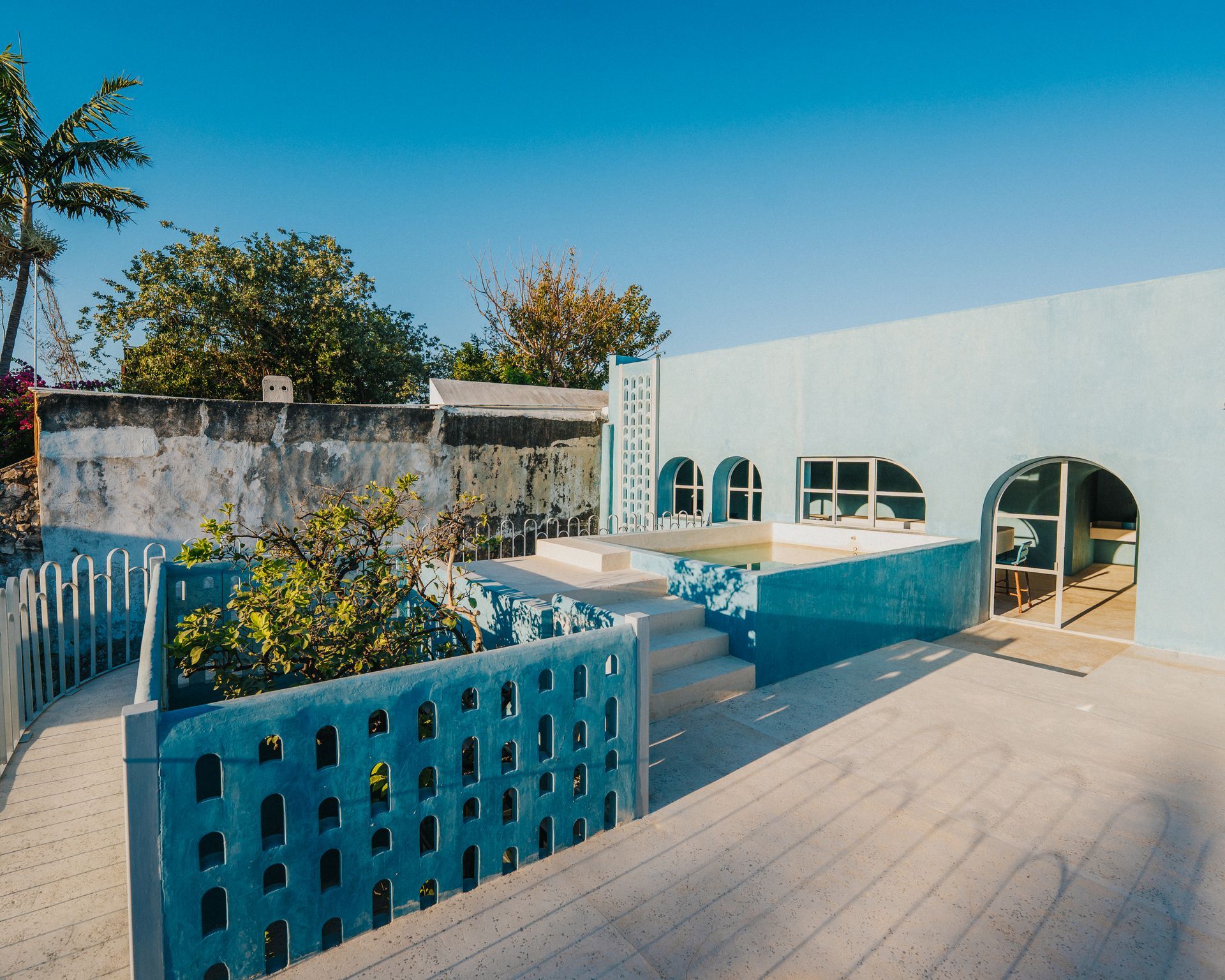 Edificio azul y blanco con piscina, palmeras y cielo azul despejado.