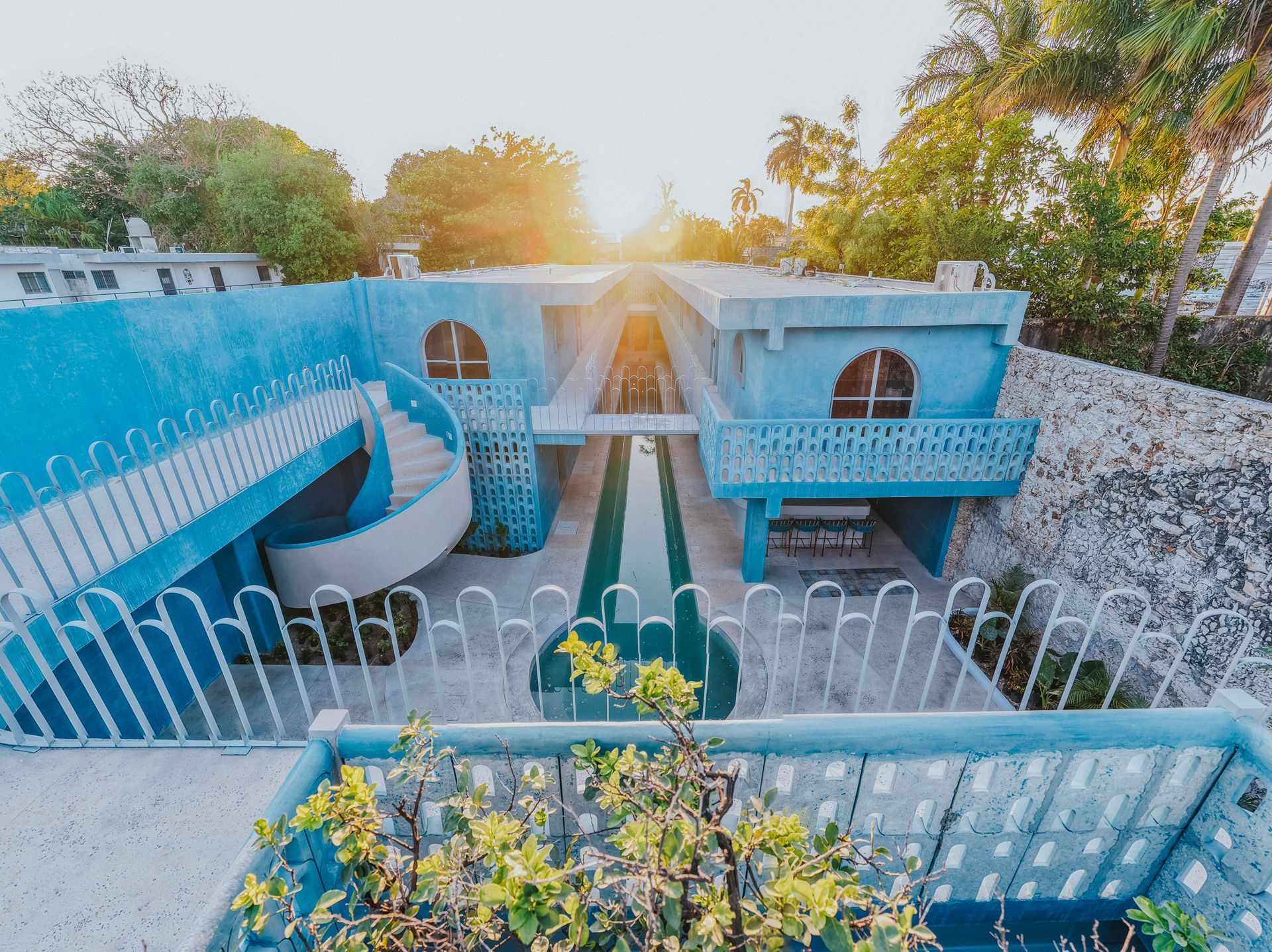 Casa modernista de color azul brillante con una escalera de caracol, una piscina alargada y una valla decorativa.