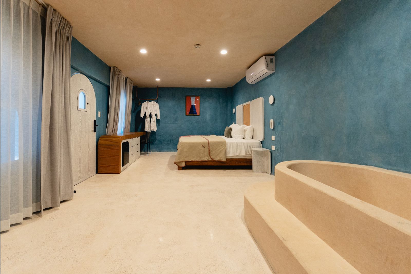 Dormitorio con cama, bañera empotrada y paredes con textura azul.