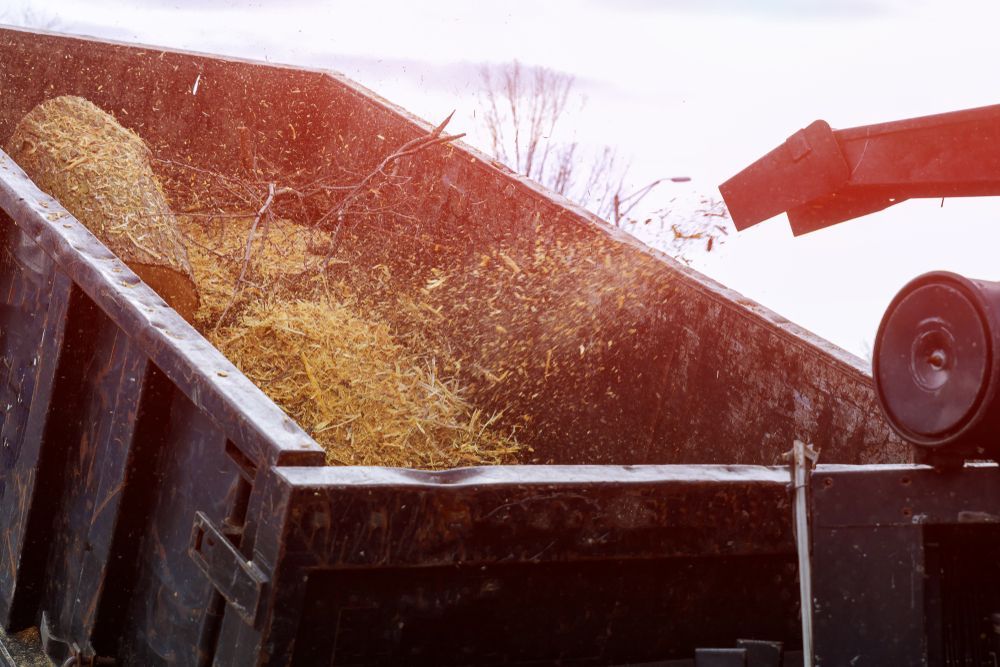 A Dumpster Filled With Hay is Being Loaded by a Tractor — All Australian Tree & Palm Services In Mount Coolum, QLD
