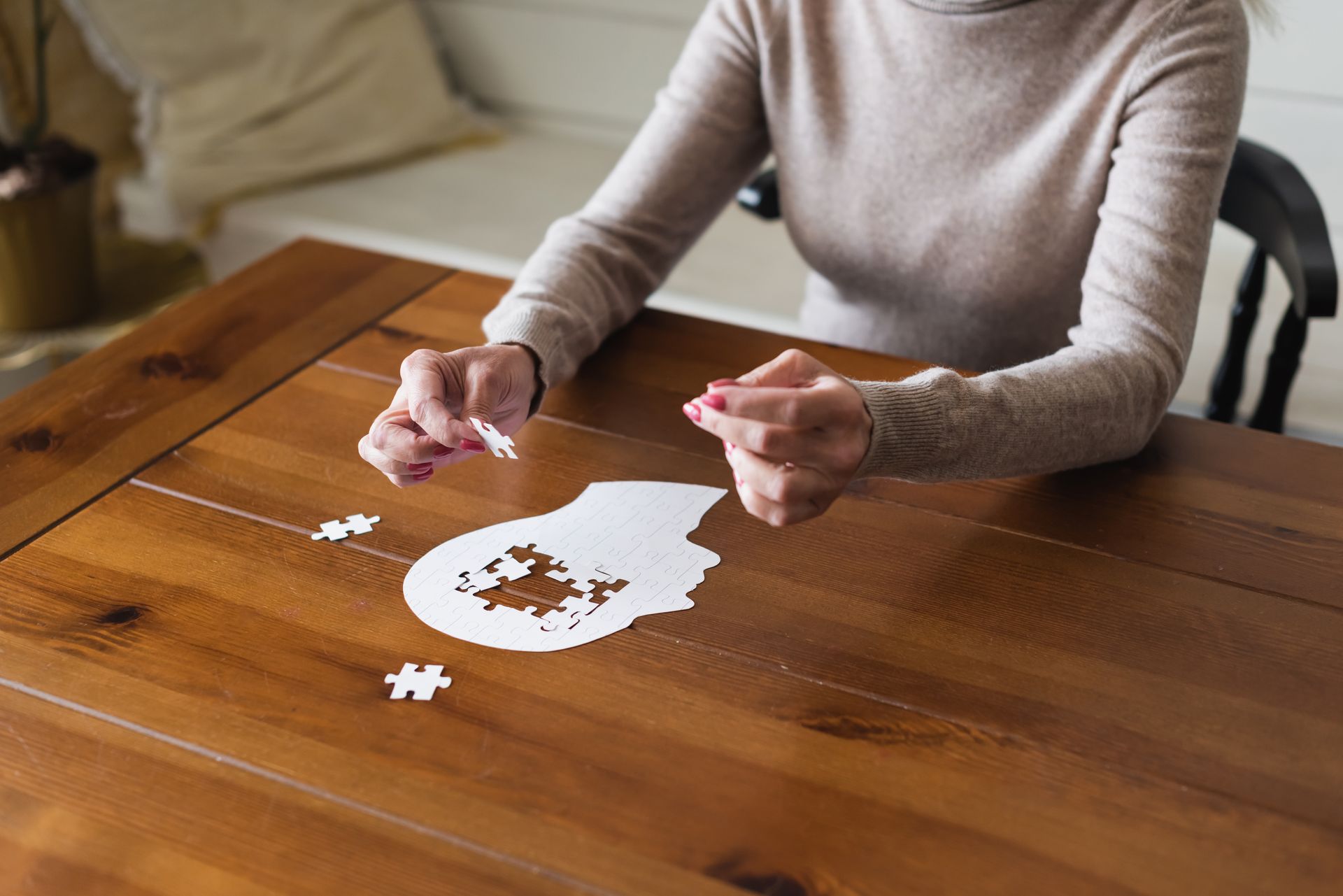 Woman fitting jigsaw puzzle pieces on a wooden table representing dementia 