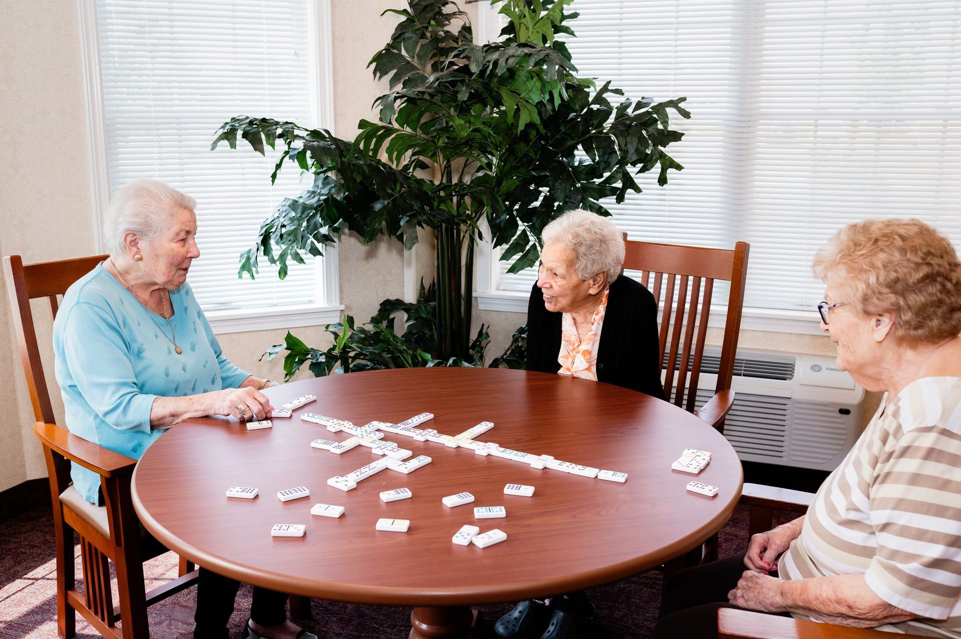 An elderly woman is sitting at a table looking out of a window.