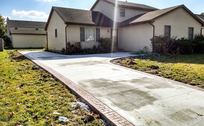 A smooth, newly poured concrete driveway with a decorative stamped brick border.