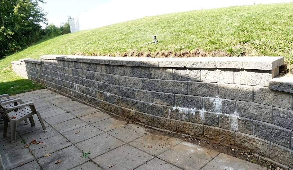 Curved concrete block retaining wall creating a flat outdoor patio space in a hilly yard.