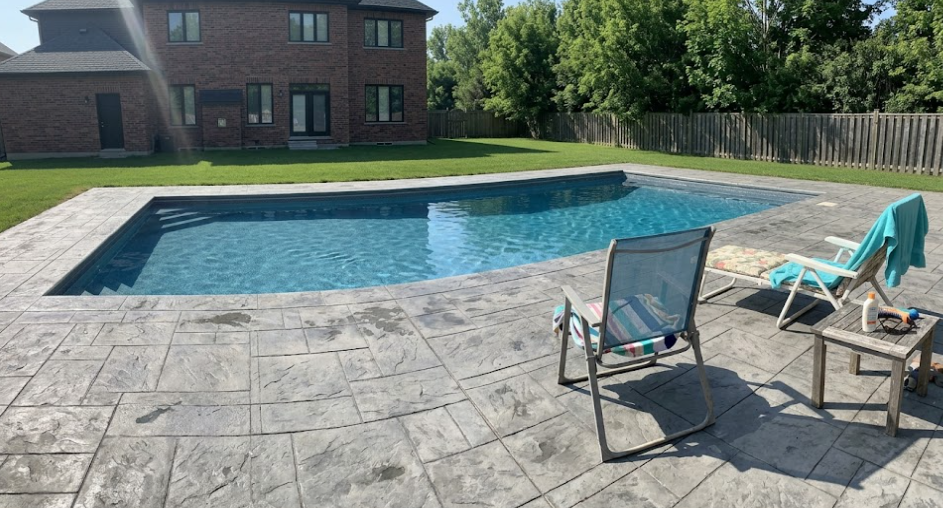 A wide view of a custom decorative concrete pool deck installation featuring a gray slate tile pattern.