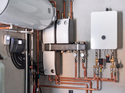 Wall-mounted boiler and hot water system with copper pipes and white tanks in a utility room