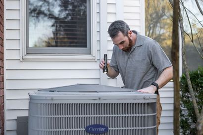 Man inspecting a Carrier air conditioner outside a house with a screwdriver in hand
