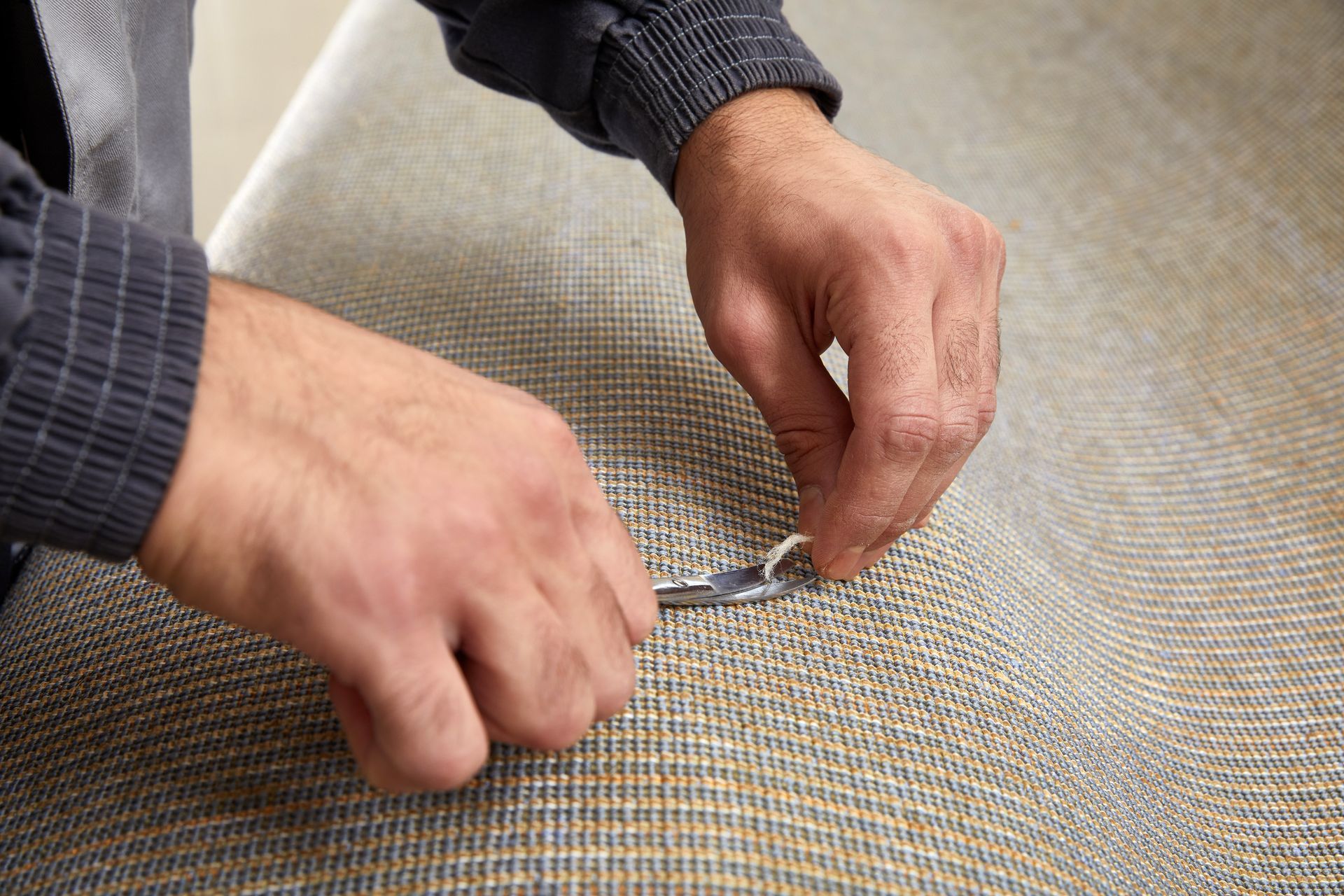 A man is fixing a carpet with a pair of scissors.