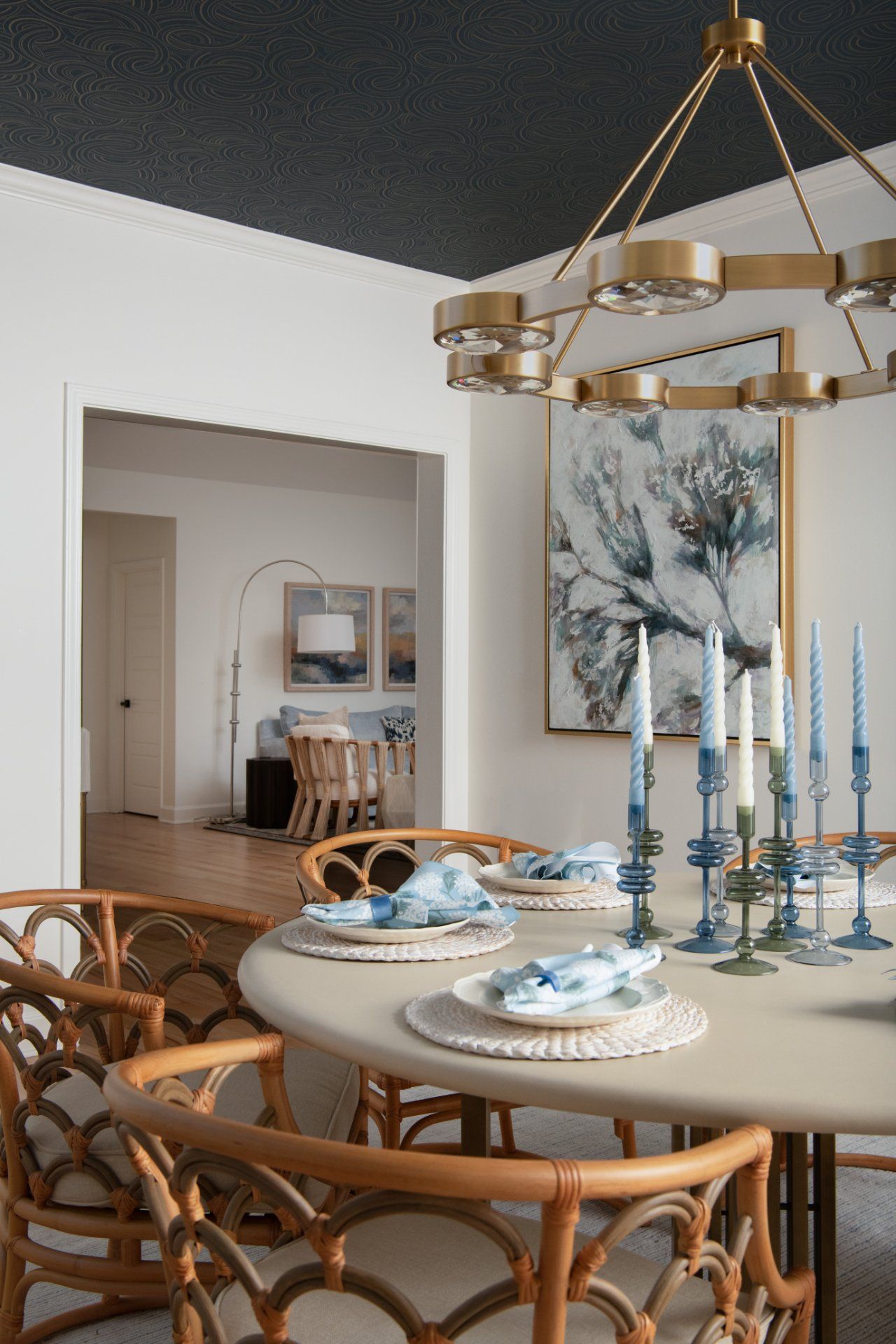 Dining room with rattan chairs, round table set with blue accents, gold chandelier, and view into an adjacent room | Charlotte, NC | An Inspiring Home