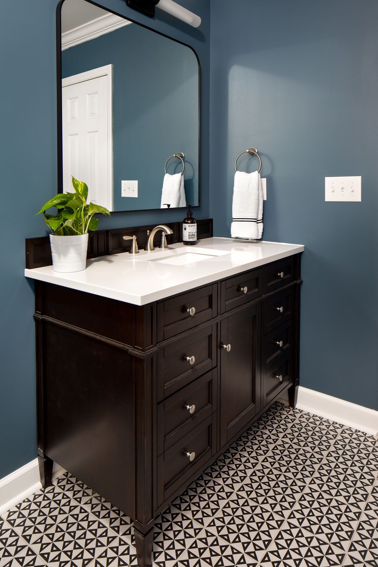 A bathroom with a sink , mirror , and black and white tile floor.