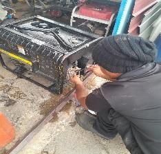 Una persona se agacha y repara una estufa o calentador de metal negro en un taller.