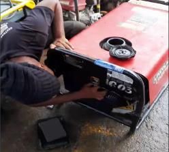 Una persona trabaja en un vehículo rojo volcado, retirando un panel trasero negro en una calle mojada.