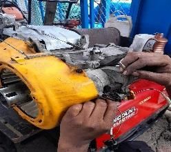 Manos reparando el motor de una motocicleta amarilla y roja en un taller.