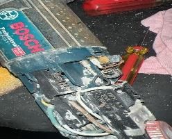 Una caja de herramientas abierta con alicates y cables sobre un banco de trabajo desordenado, junto a un destornillador de mango rojo.