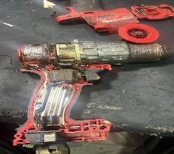 Taladro eléctrico inalámbrico rojo y gris con sus accesorios sobre una superficie de trabajo oscura, cubierta de polvo.