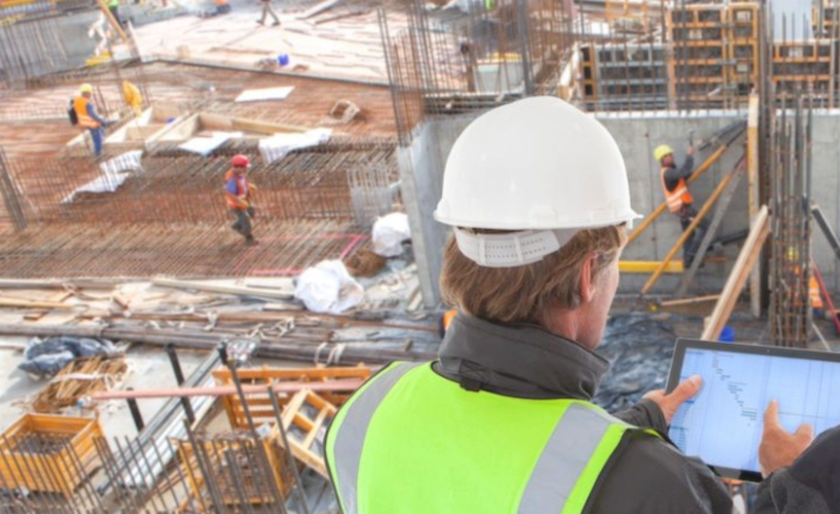Un trabajador de la construcción está mirando una tableta en un sitio de construcción.