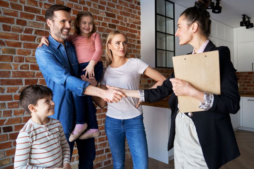 Family greeting a woman at a doorway, smiling and shaking hands in a bright hallway