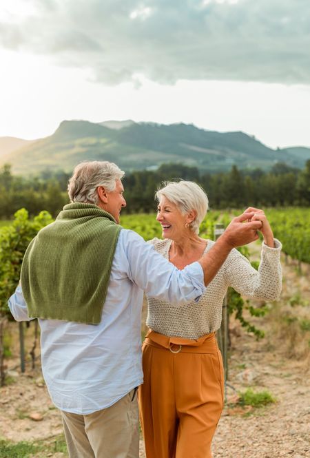 Two people dancing in a vineyard with mountains and cloudy sky in the background