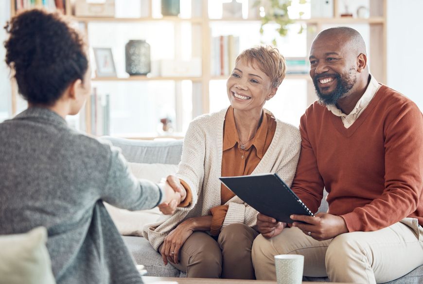Three people in a living room shaking hands during a meeting, with one holding a tablet.