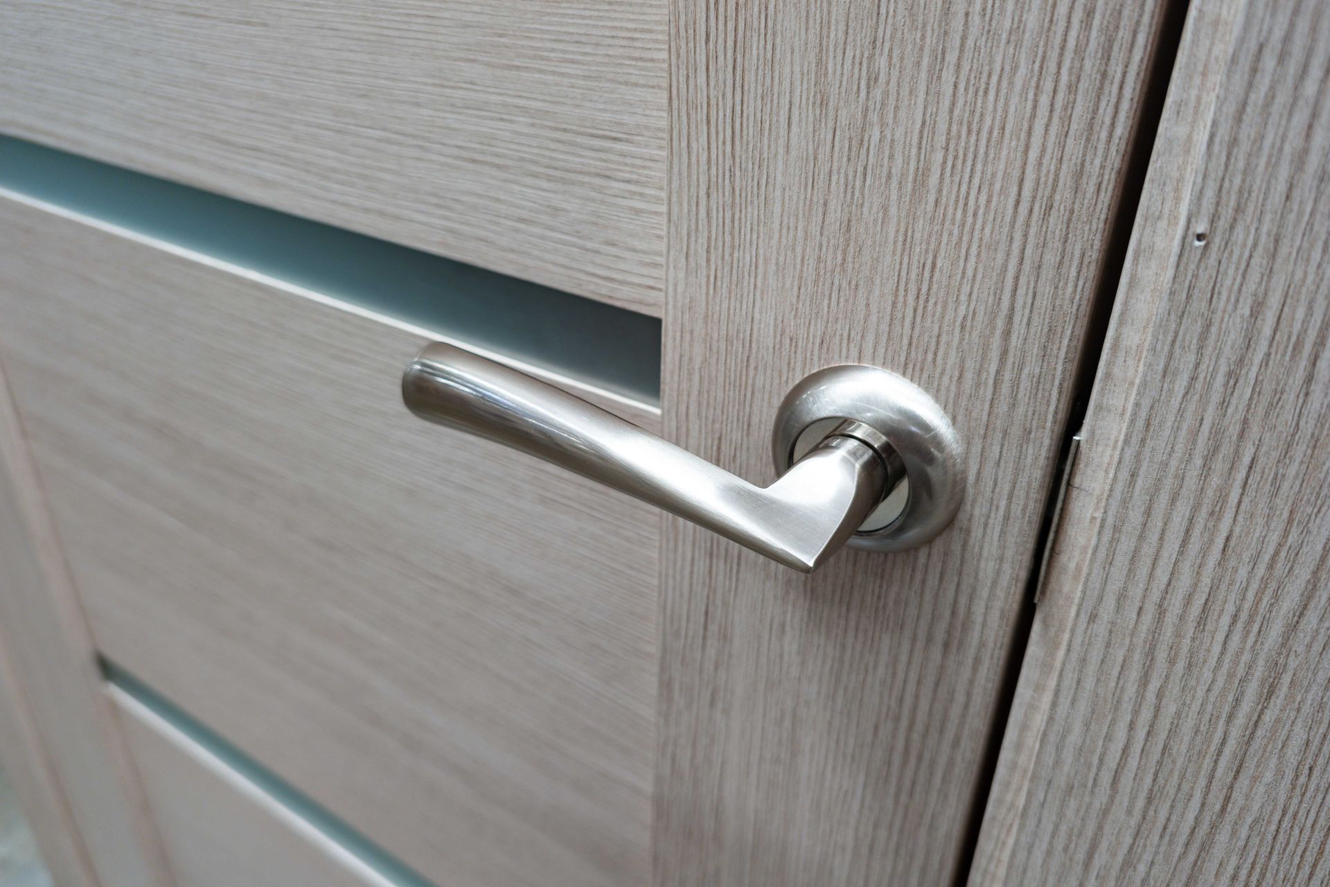 Gros plan sur une poignée de porte argentée sur une porte en bois gris clair