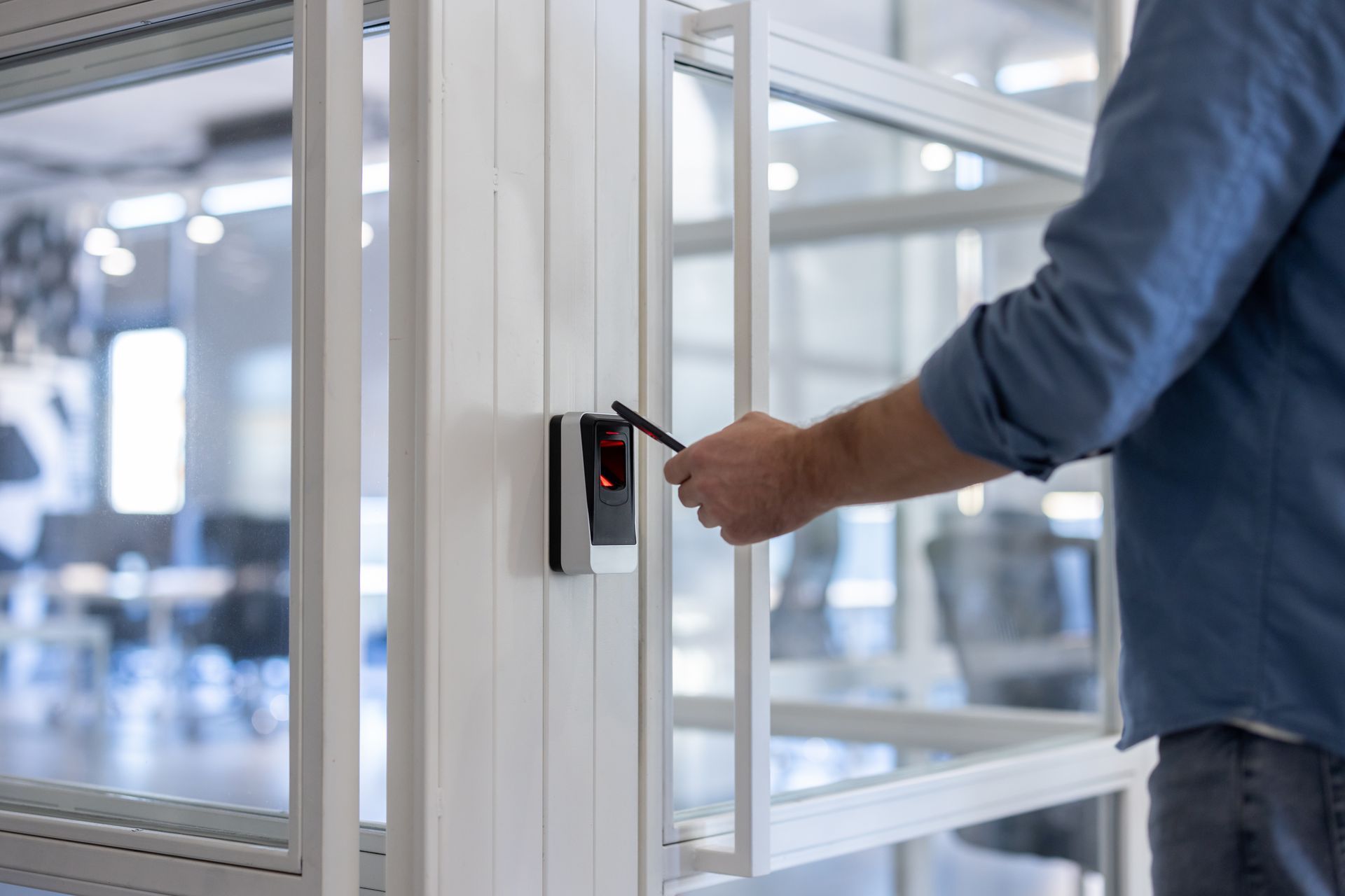 Une personne utilise un lecteur de badge pour ouvrir une porte de bureau vitrée.