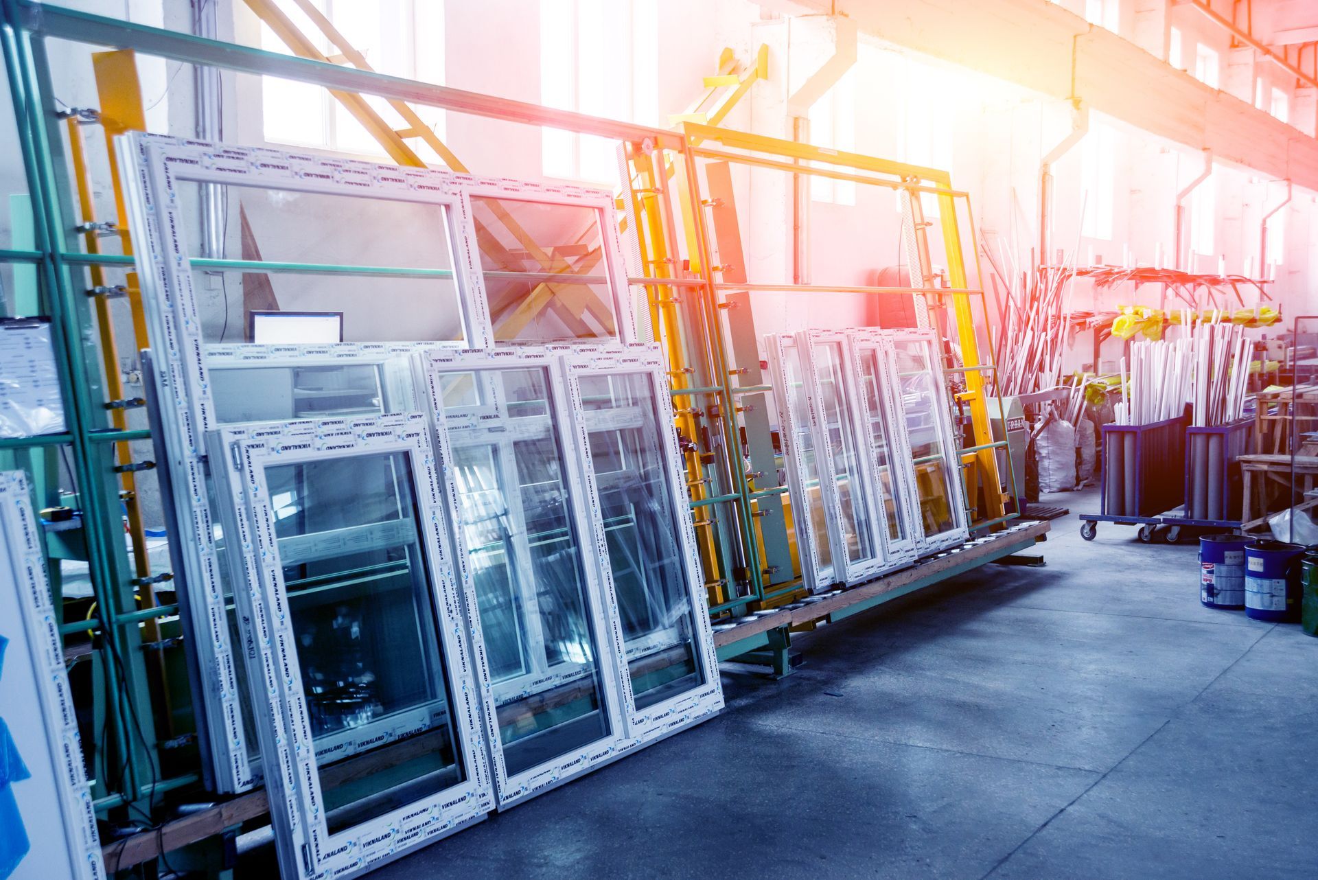 Dans un atelier ou un entrepôt lumineux, des rangées de vitrines industrielles sont éclairées par la chaude lumière du soleil.
