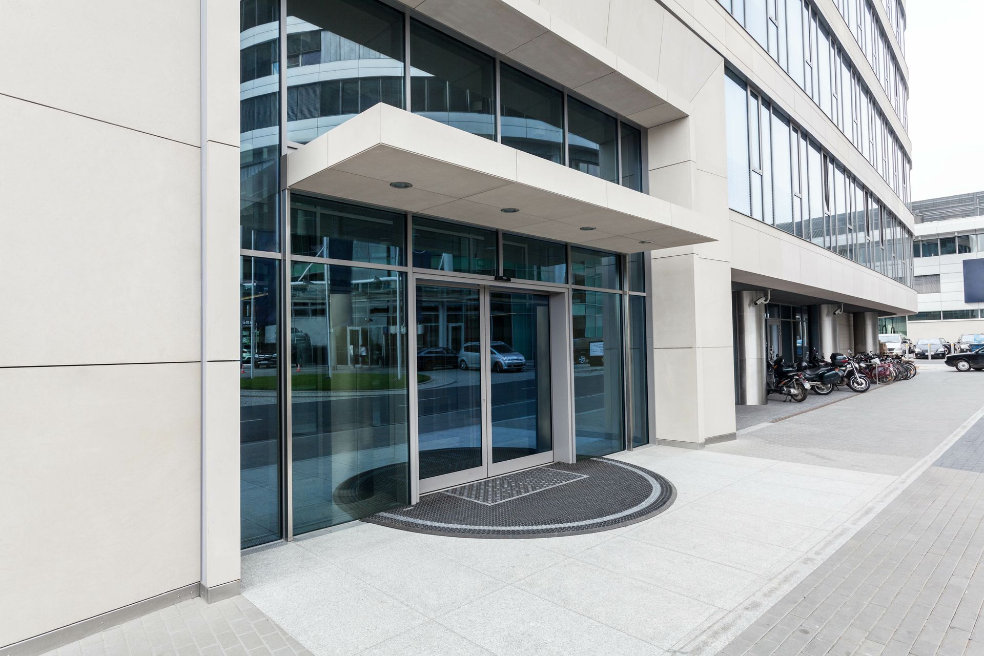 Entrée d'un immeuble de bureaux moderne avec portes vitrées et auvent couvert donnant sur un trottoir