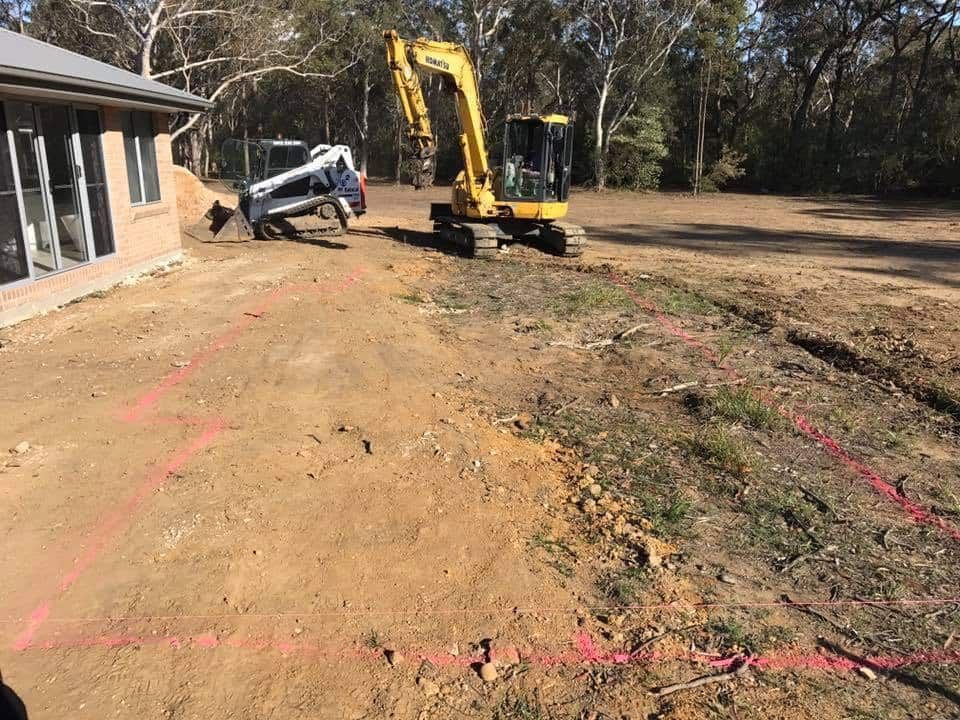 A Yellow Excavator is Driving Down a Dirt Road Next to a House