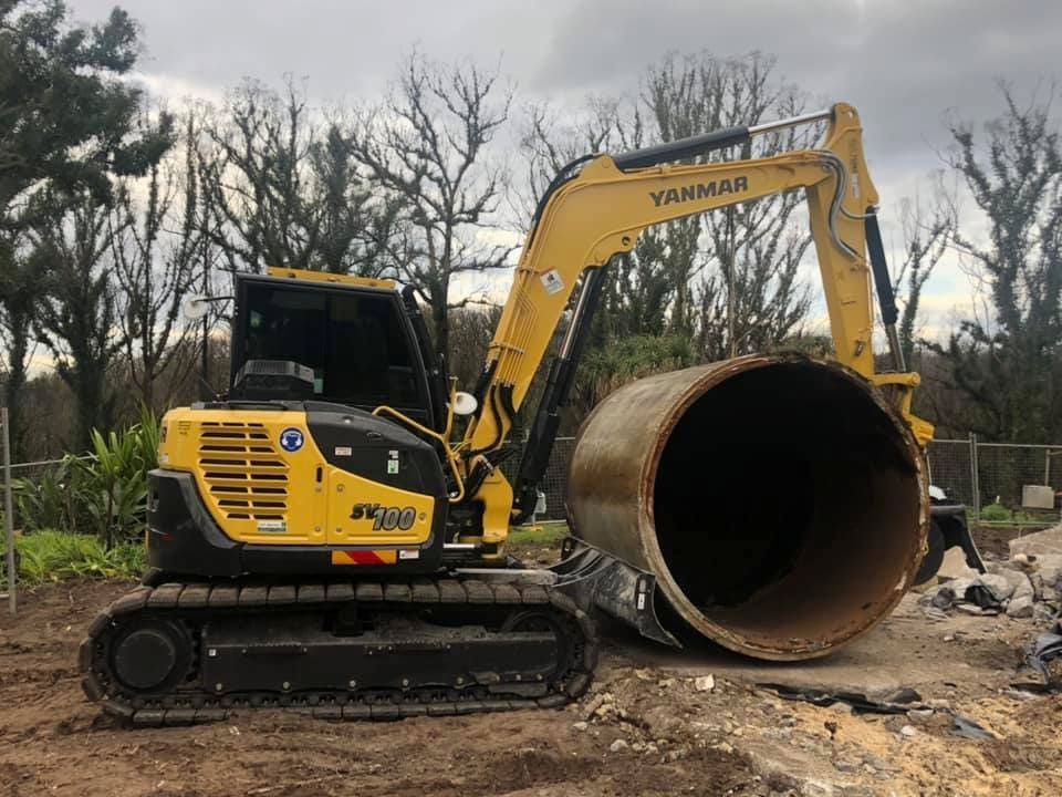 A Yellow Excavator is Cutting a Large Pipe in a Dirt Field — BeCivil in Tomerong, NSW