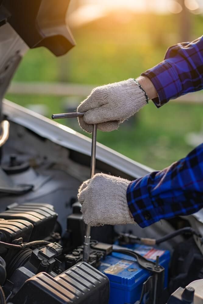 A Man Is Working On The Engine Of A Car With A Wrench — Coast 2 Coast Batteries in Terrigal, NSW