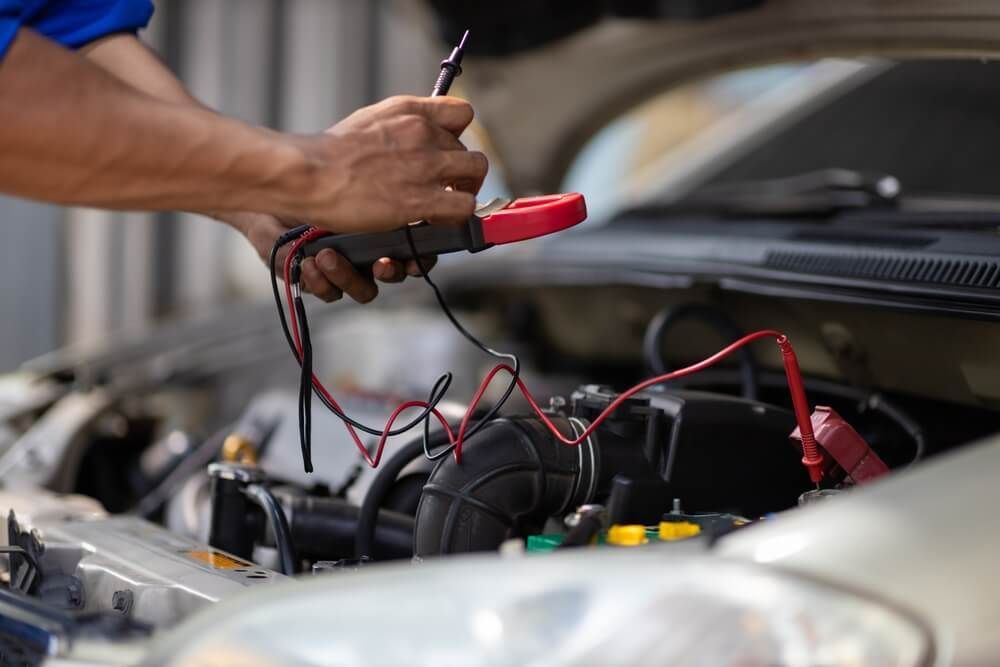 A Man Is Working On The Engine Of A Car With A Multimeter — Coast 2 Coast Batteries in West Gosford, NSW