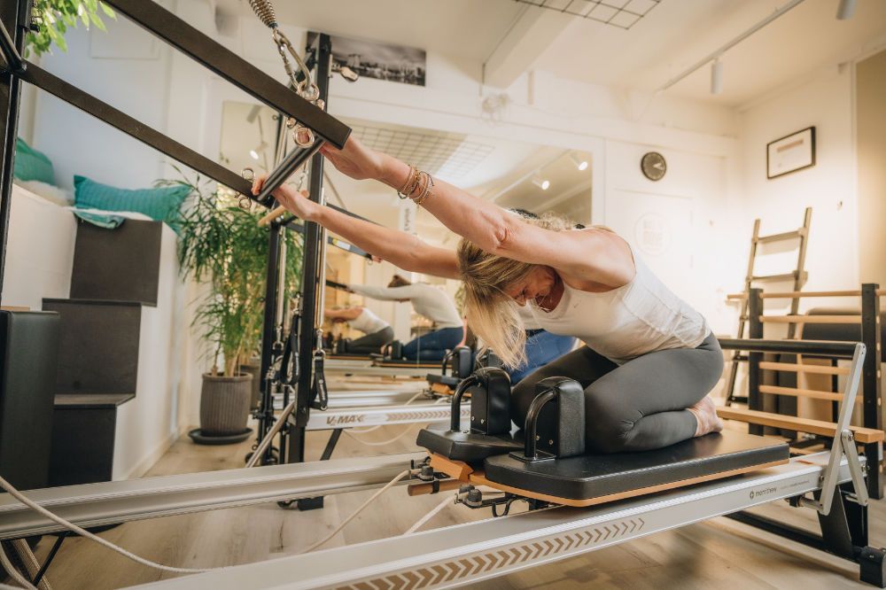 A woman is helping a man stretch his leg on a pilates cadillac