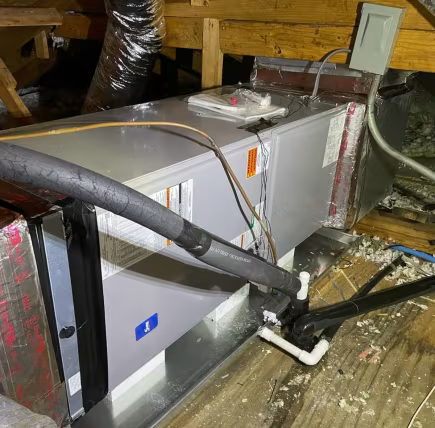 Gray HVAC unit in a cramped attic, surrounded by insulated ducts and water on the floor