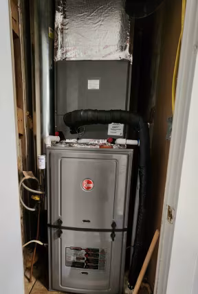 Furnace and HVAC unit in a narrow utility closet with exposed ductwork and insulation.