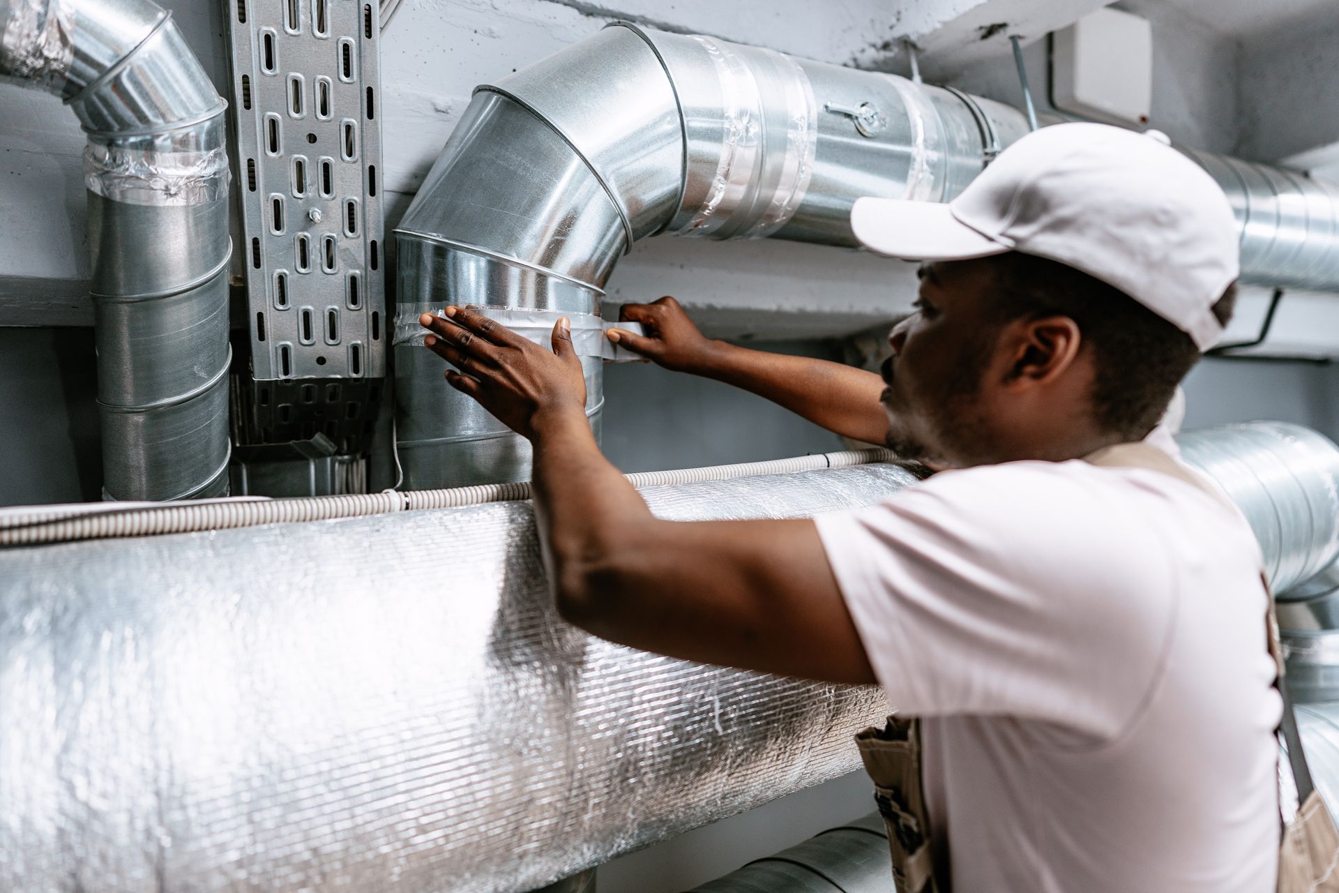 Worker adjusting silver HVAC duct insulation in an industrial setting