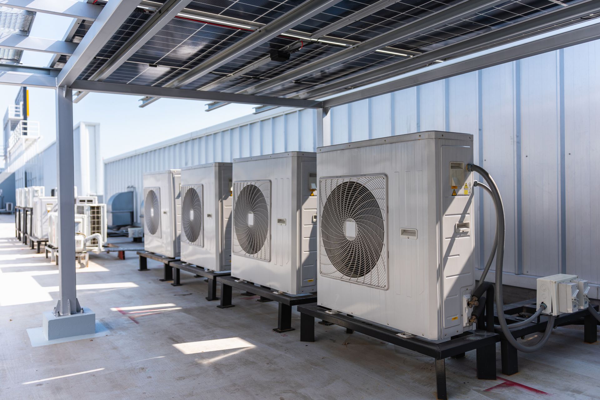 Row of rooftop HVAC units with large fans beneath metal shade canopy