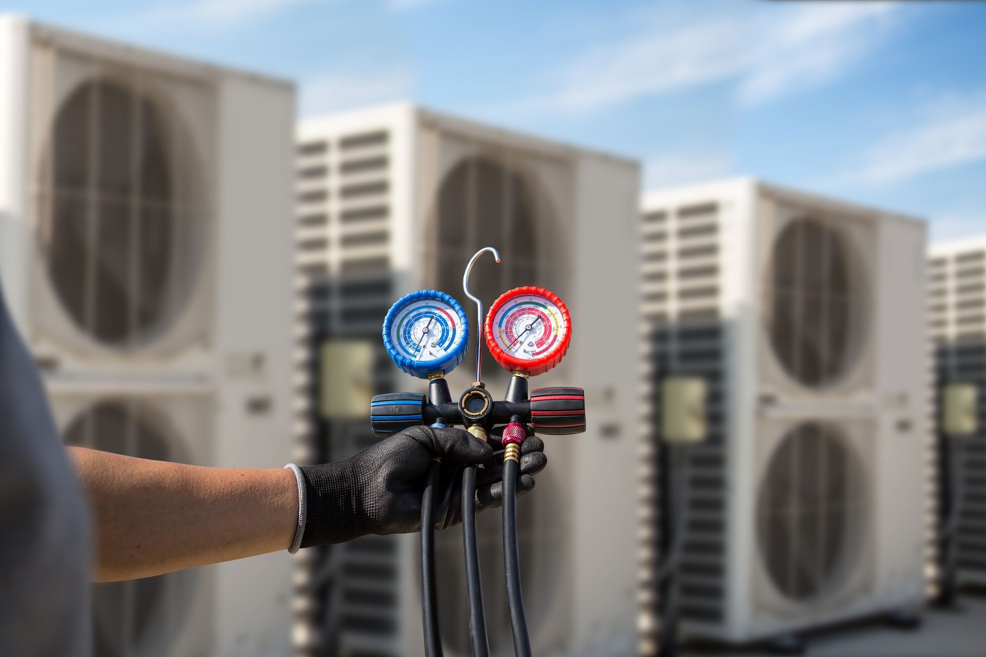 Technician holding HVAC manifold gauges in front of rooftop air conditioning units