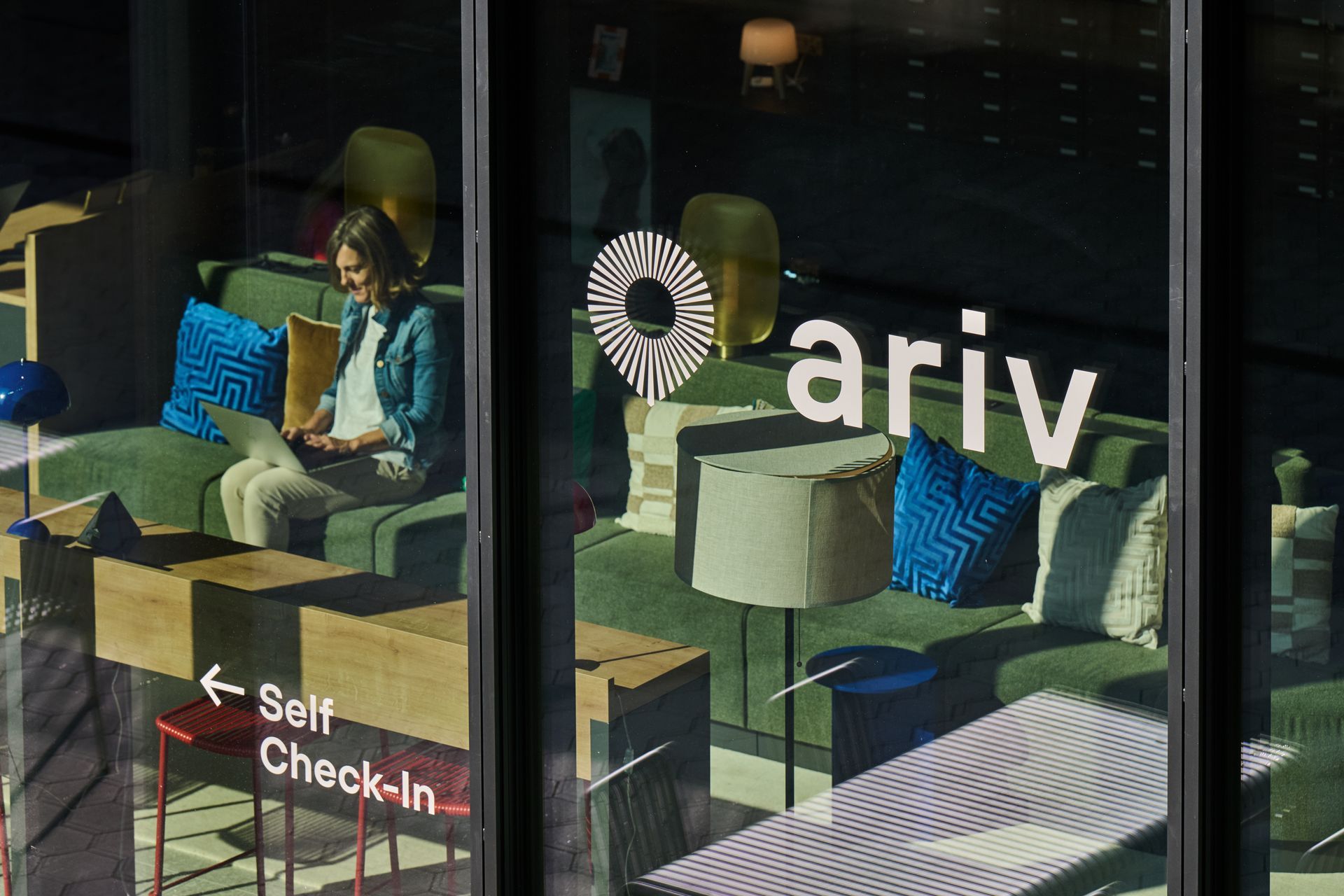 Interior of ariv self check-in lounge with chairs, tables, and a person sitting by the window